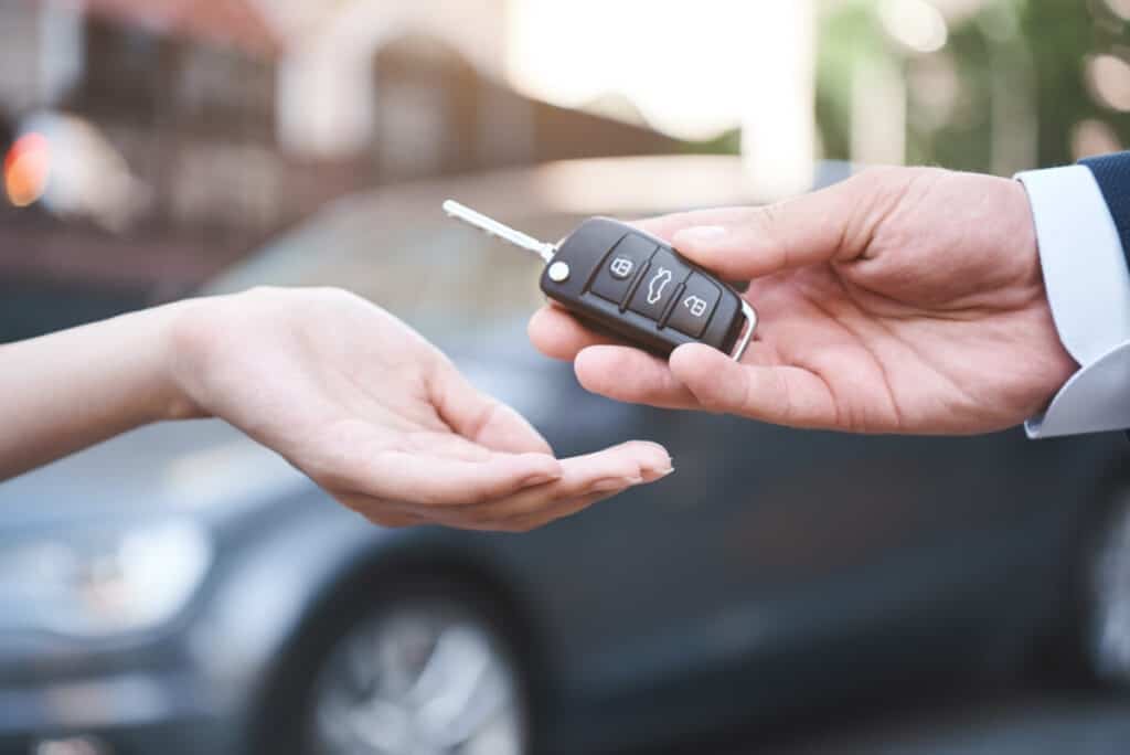 When is the best time to buy a car? The image shows a male hand giving a car key to a female hand