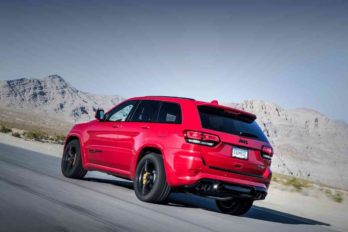 Image for Which Jeep Grand Cherokee Has Dual Exhaust? shows a red Grand Cherokee trackhawk driving at speed. The background is a series of deserted mountains