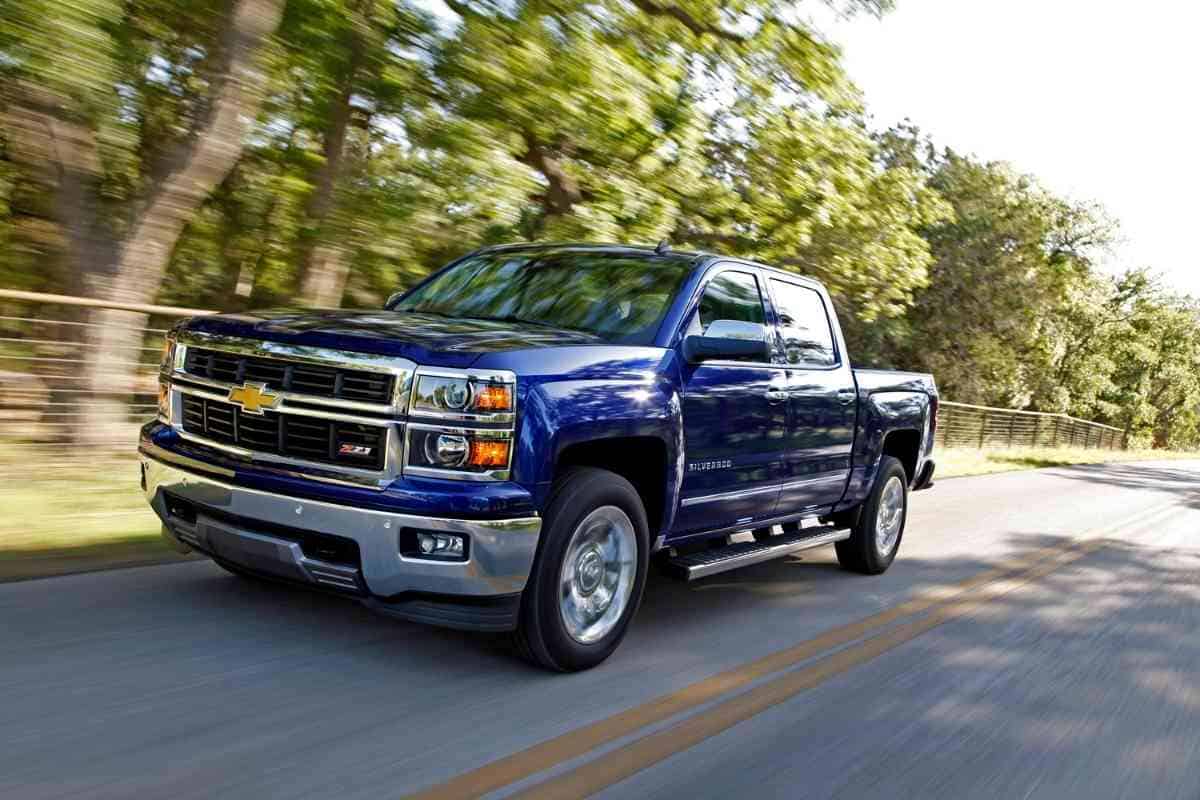 Image for: Best and Worst Chevy Silverado years shows a blue Chevy 1500 against a forested road
