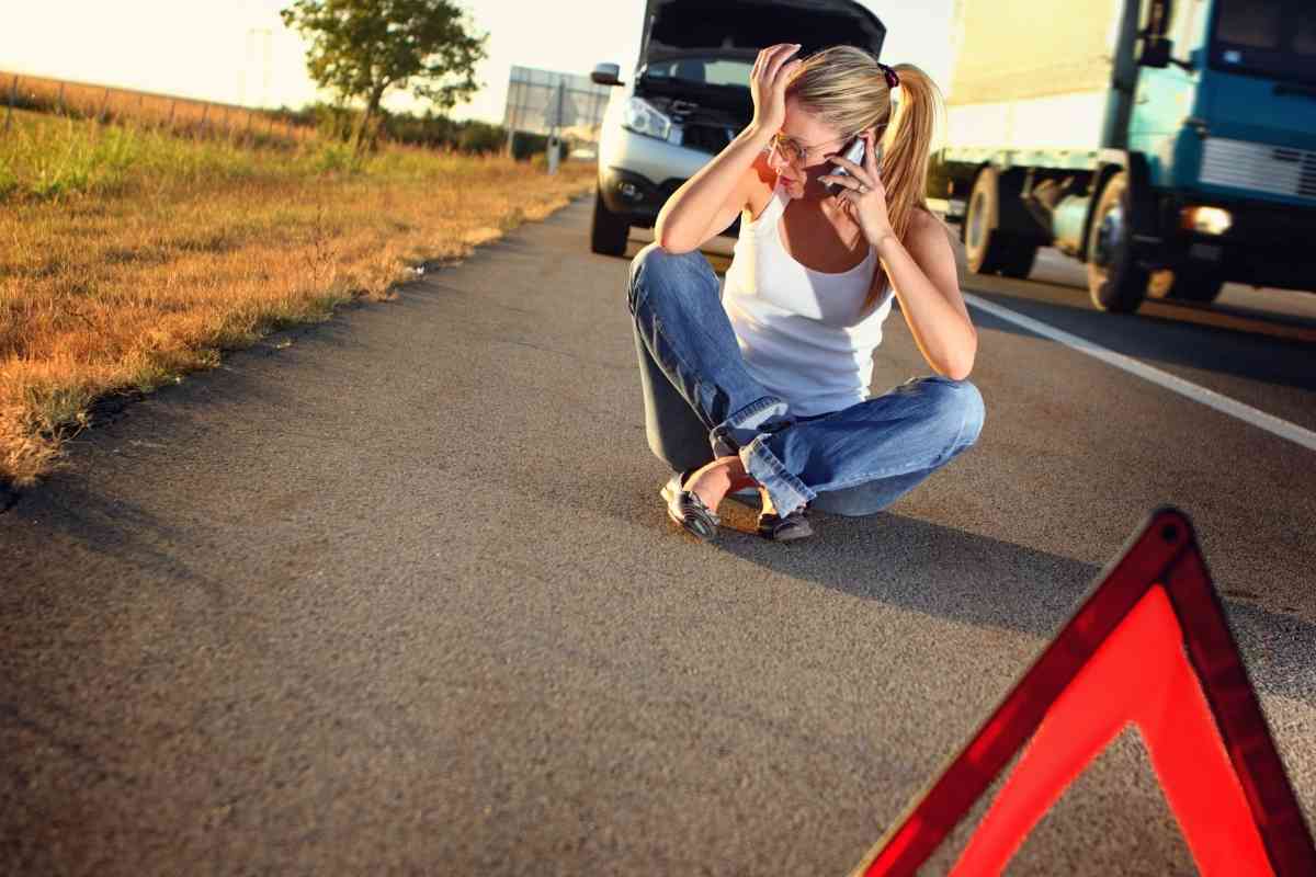 Image for: Is an Extended Car Warranty Worth It? shows a woman cross legged on the road, with a warning triangle and a broken down car