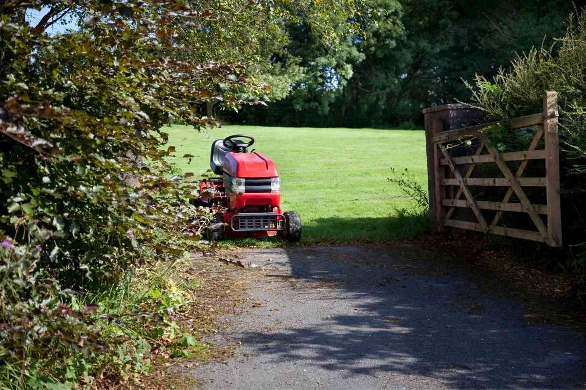 Image for: Will A Riding Lawn Mower Fit In A Pickup Truck shows a parked red riding lawn mower in a wide grassy field, next to a wooden entrance