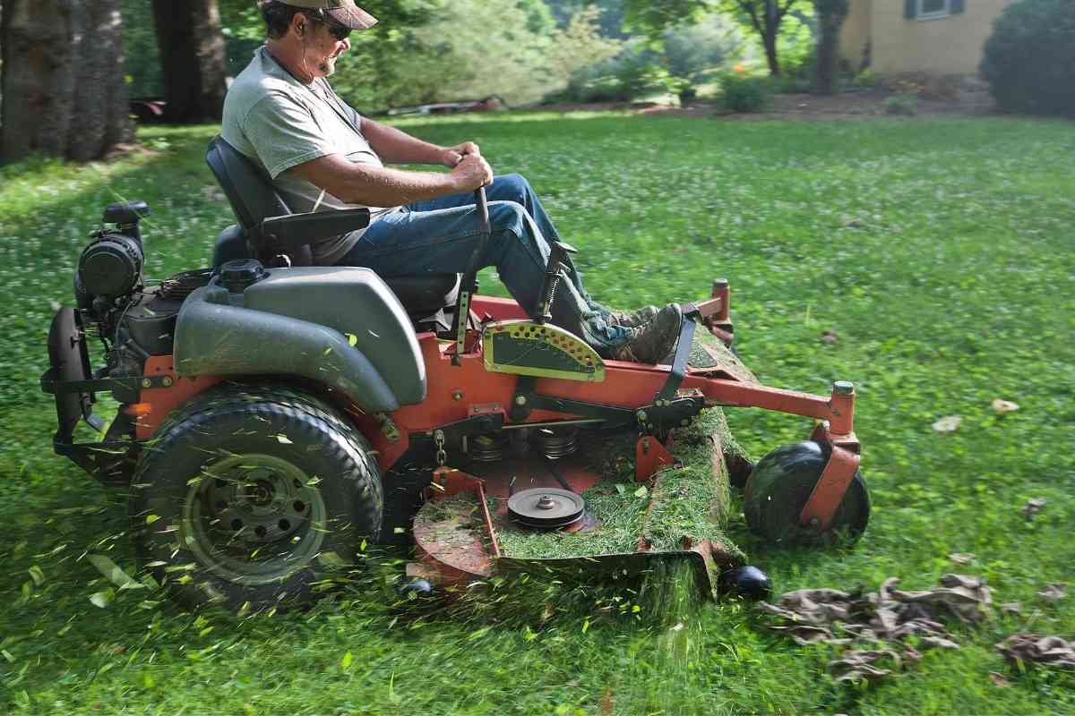 Image for "Will a riding lawn mower fit in a pickup truck?" shows a riding lawn mower cutting grass, with a man operating it. He's wearing sunglasses and a hat
