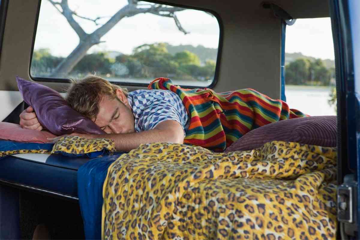 Image for: will a full mattress fit in a Dodge Caravan? Shows a man sleeping in the back of a vehicle, with a clear background