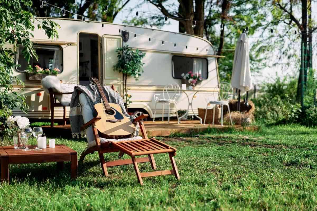 Image for: What Size Truck Do You Need To Pull A 40-Foot Camper? Shows a generic countryside image of a seat with a guitar on top, and a camper in the background, with forest surrounding it