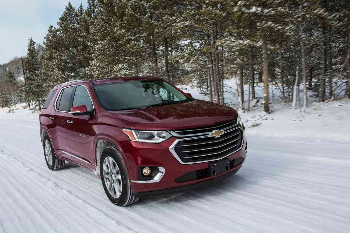 What Are The Chevy Traverse Years To Avoid? The image shows a burgundy Chevy Traverse going through snow, and the background has blurry trees