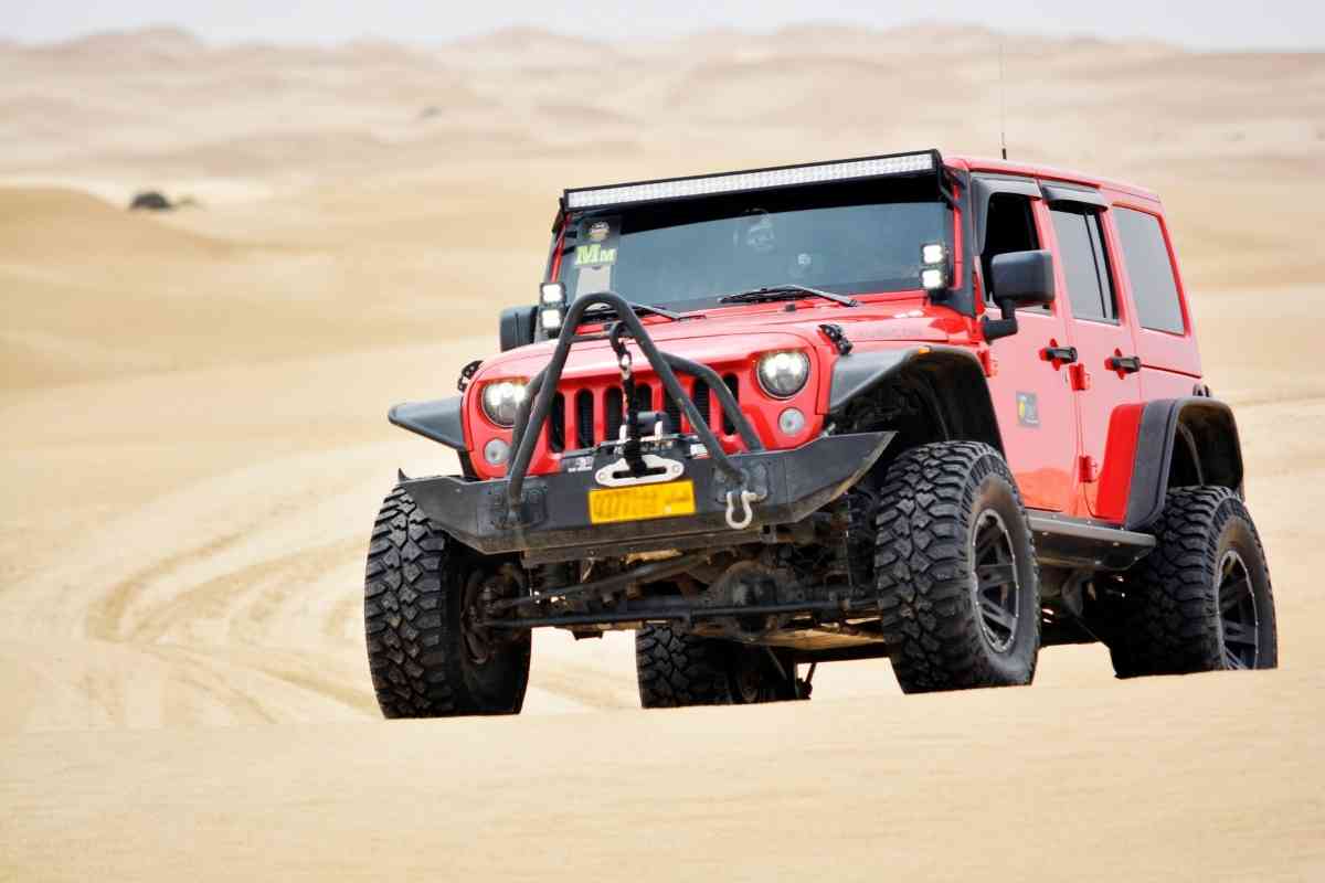 Image for: Difference between 33 and 35 inch tires shows a lifted red Jeep Wrangler, in desert sand. 