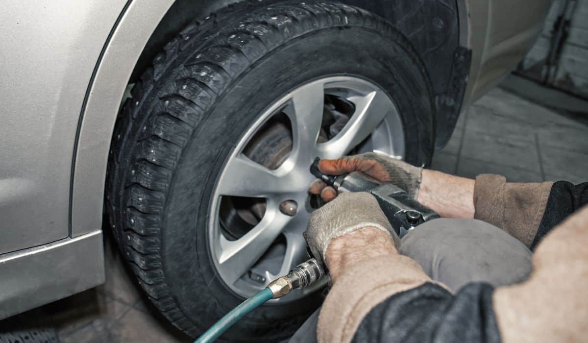 Car mechanic worker doing tire or wheel replacement with pneumatic wrench in garage of repair service station