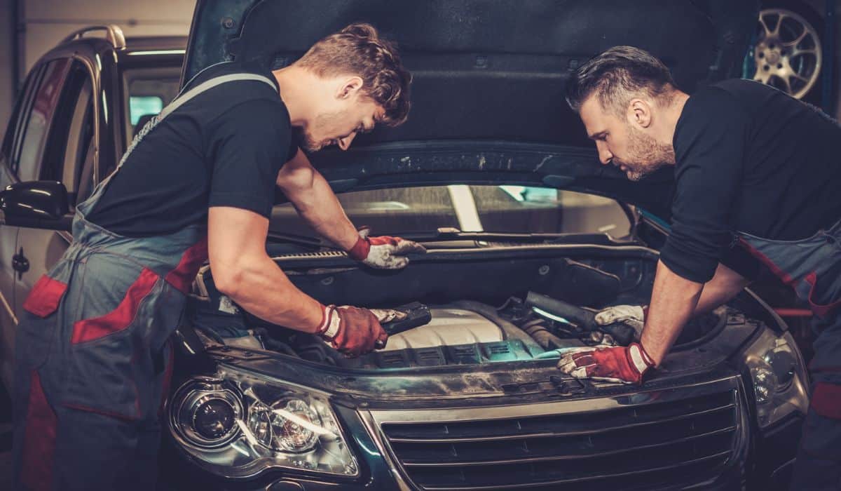 Car mechanics checking under hood in auto repair service