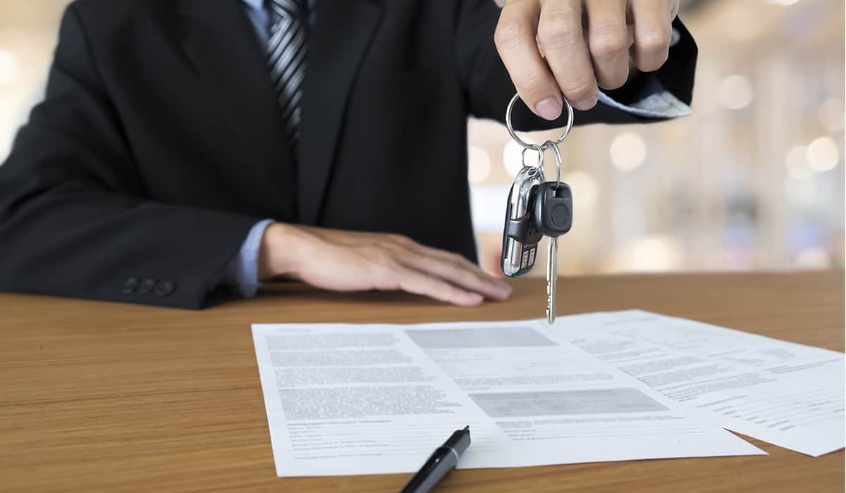 Car sale, business man hands over keys across table full of papers