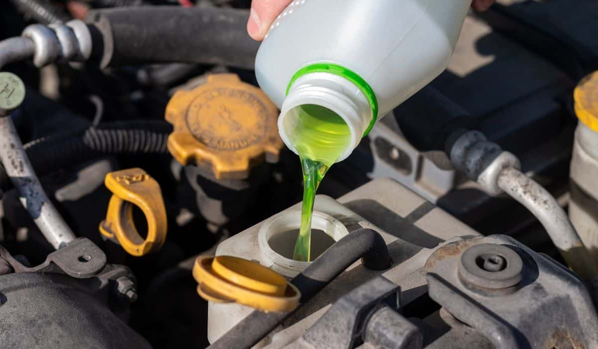 Hand with bottle pouring antifreeze coolant into the expansion tank