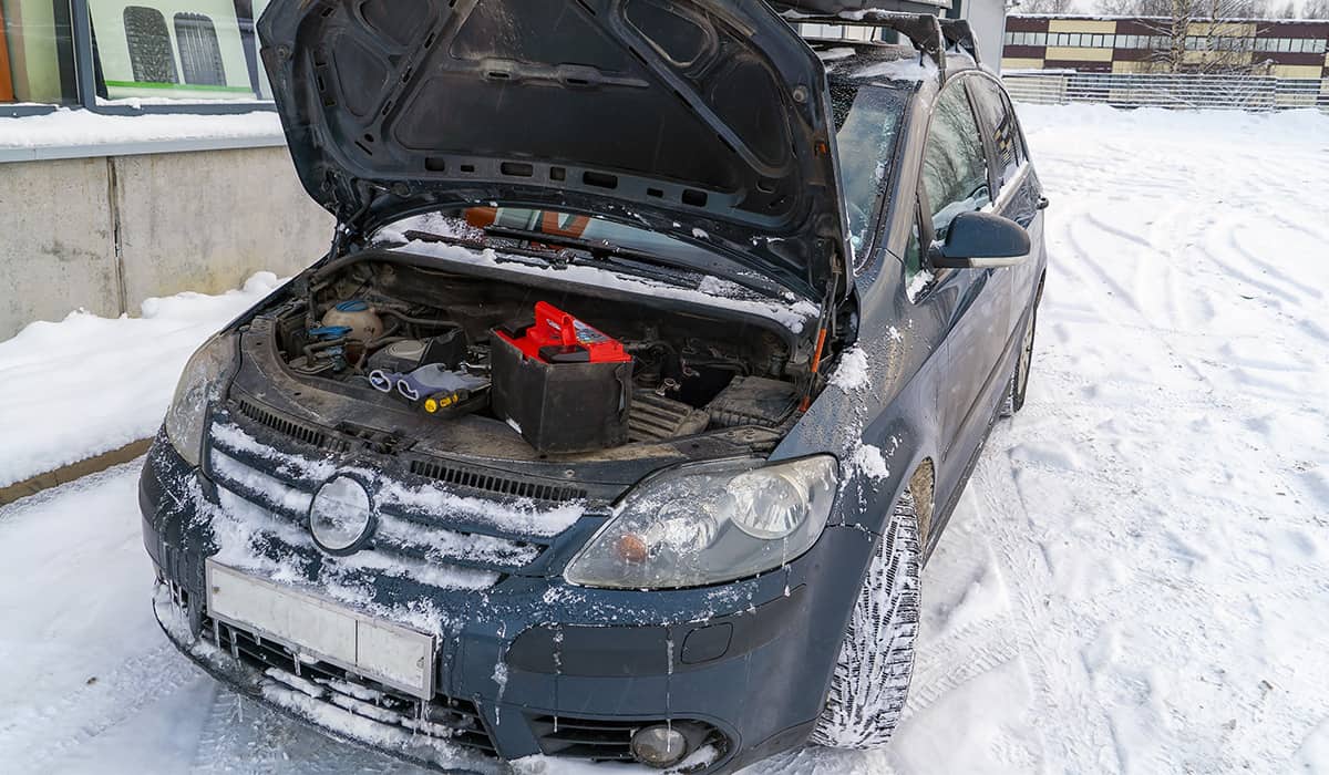 Car covered in ice and snow with the hood open, showing a removed battery and automobile tools