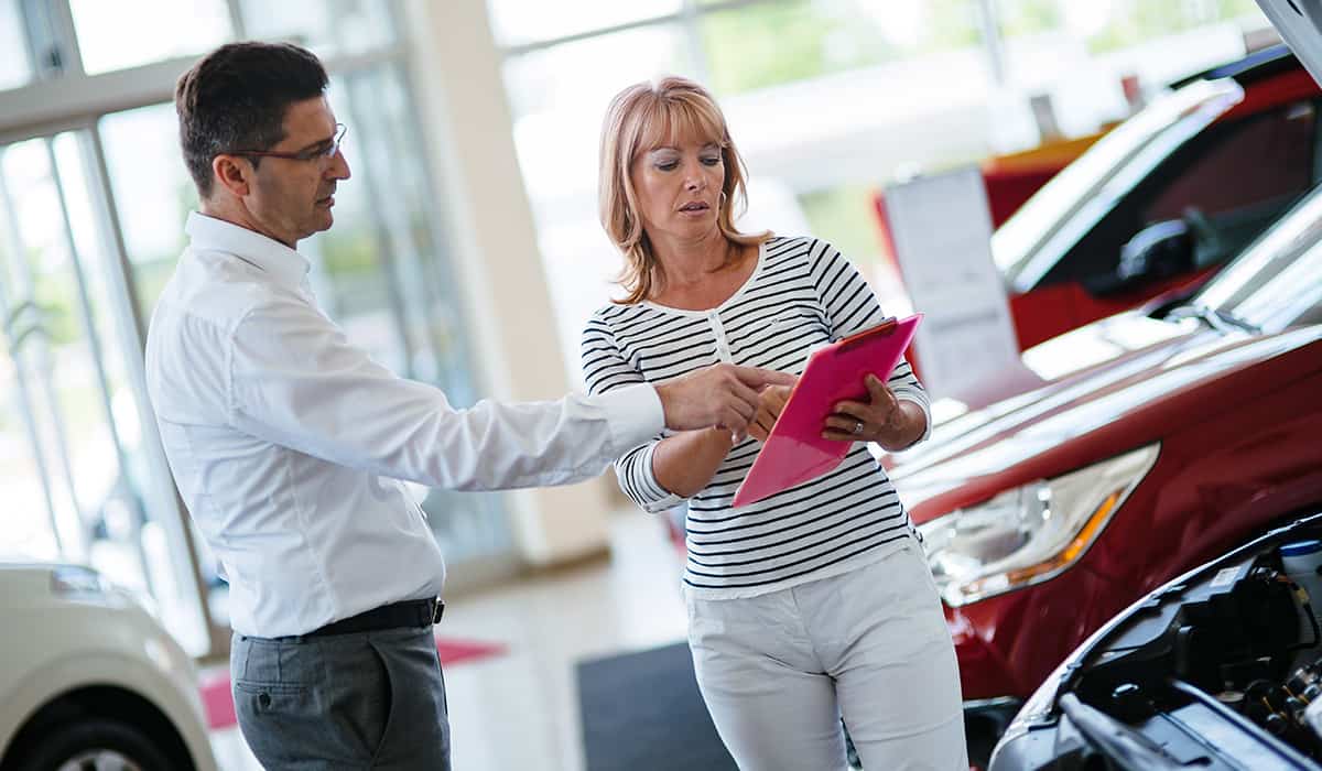 Man pointing to clipboard held by a woman in a car dealership