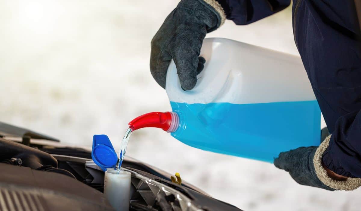 Man with gloves pouring antifreeze coolant into car reservoir in winter season