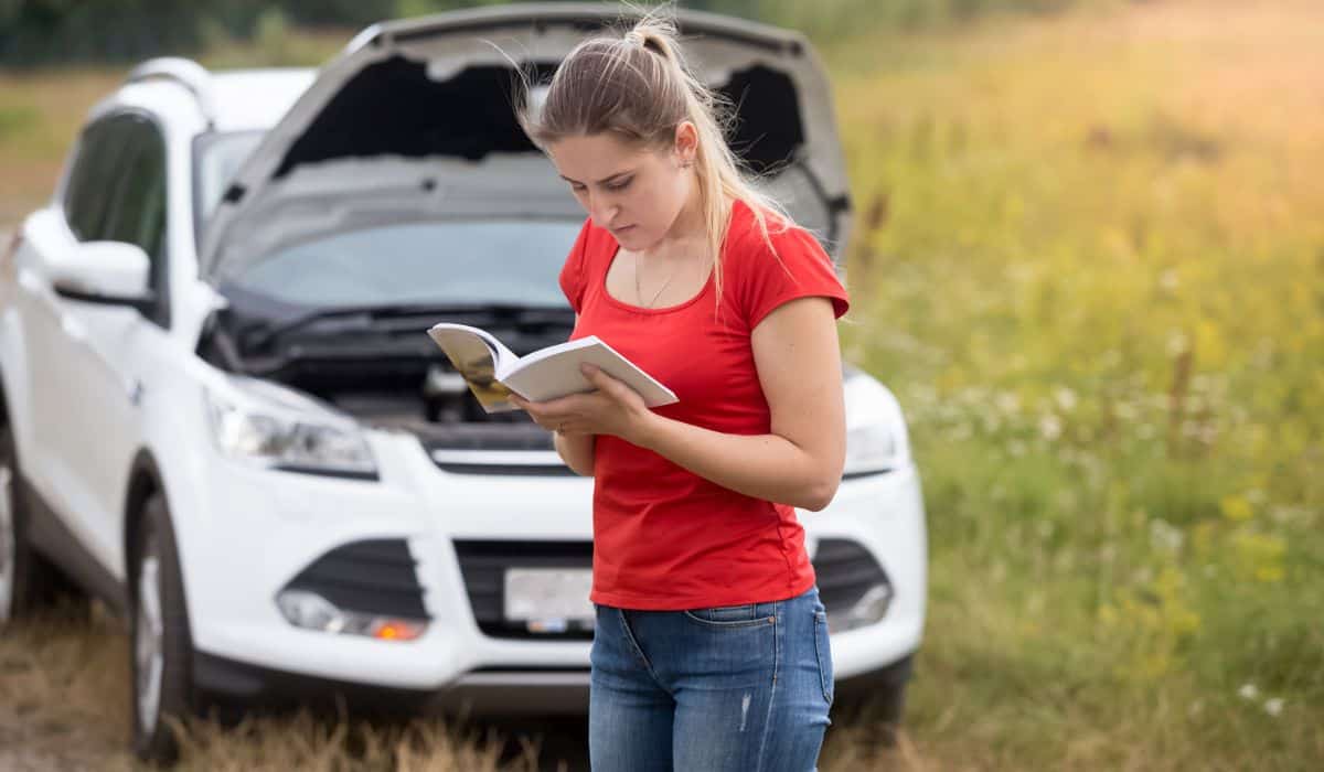 Portrait of stressed woman standing at broken car and reading ow