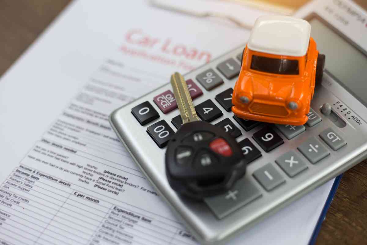 Image for: should you buy a new or used car? shows a small toy car over a calculator, and a car key, above a car loan statement