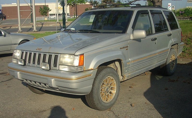 A wornout 1995 Jeep Grand Cherokee with golden rims, in an urban environment