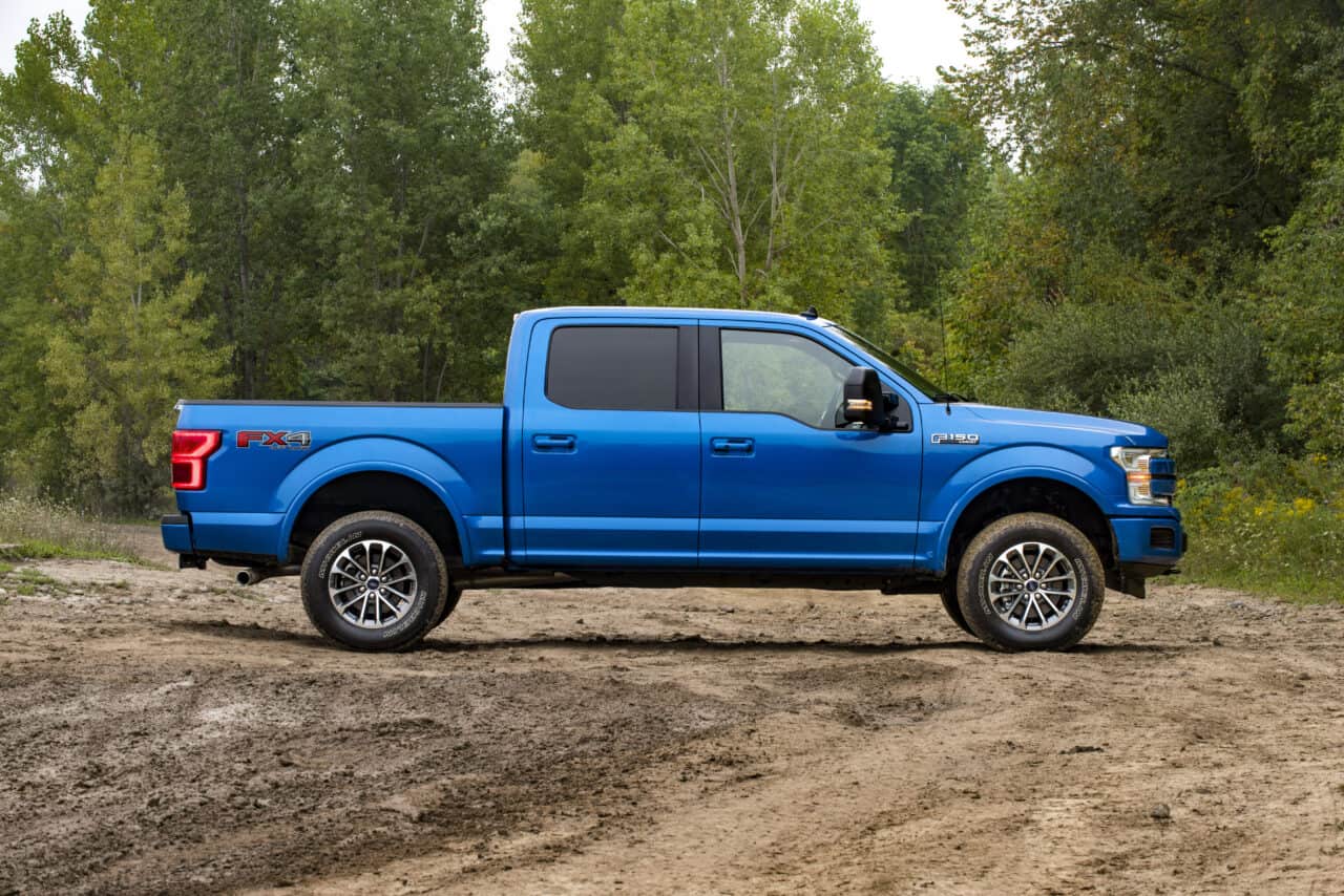 A blue Ford F-150 from the side. It is on muddy roads, in front of trees, standing still. It's an example image for the article on how much do pickup trucks weigh

