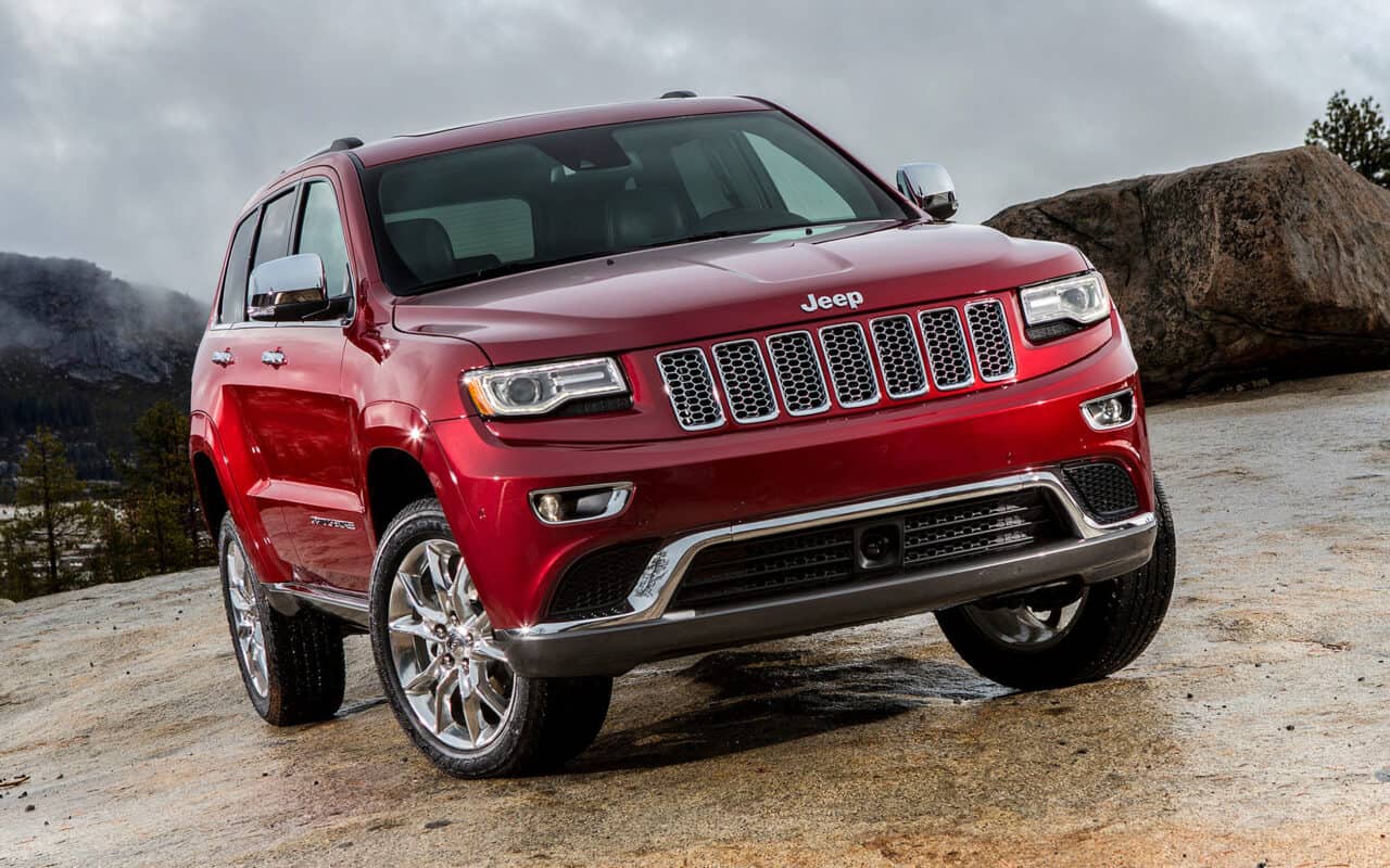 A red 2013 Jeep Grand Cherokee at an incline against a rocky background