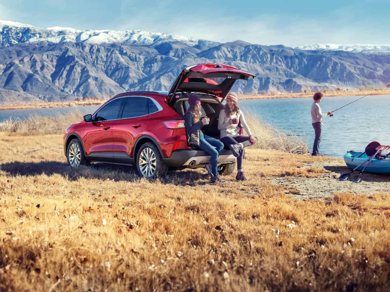 Image for: towing with a Ford escape shows two women resting in the back of a red Ford Escape, while a man is fishing in the background. 