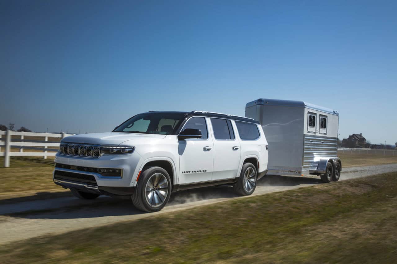 photo of a 2025 Jeep Grand Wagoneer pulling a horse trailer down a gravel road along a farm