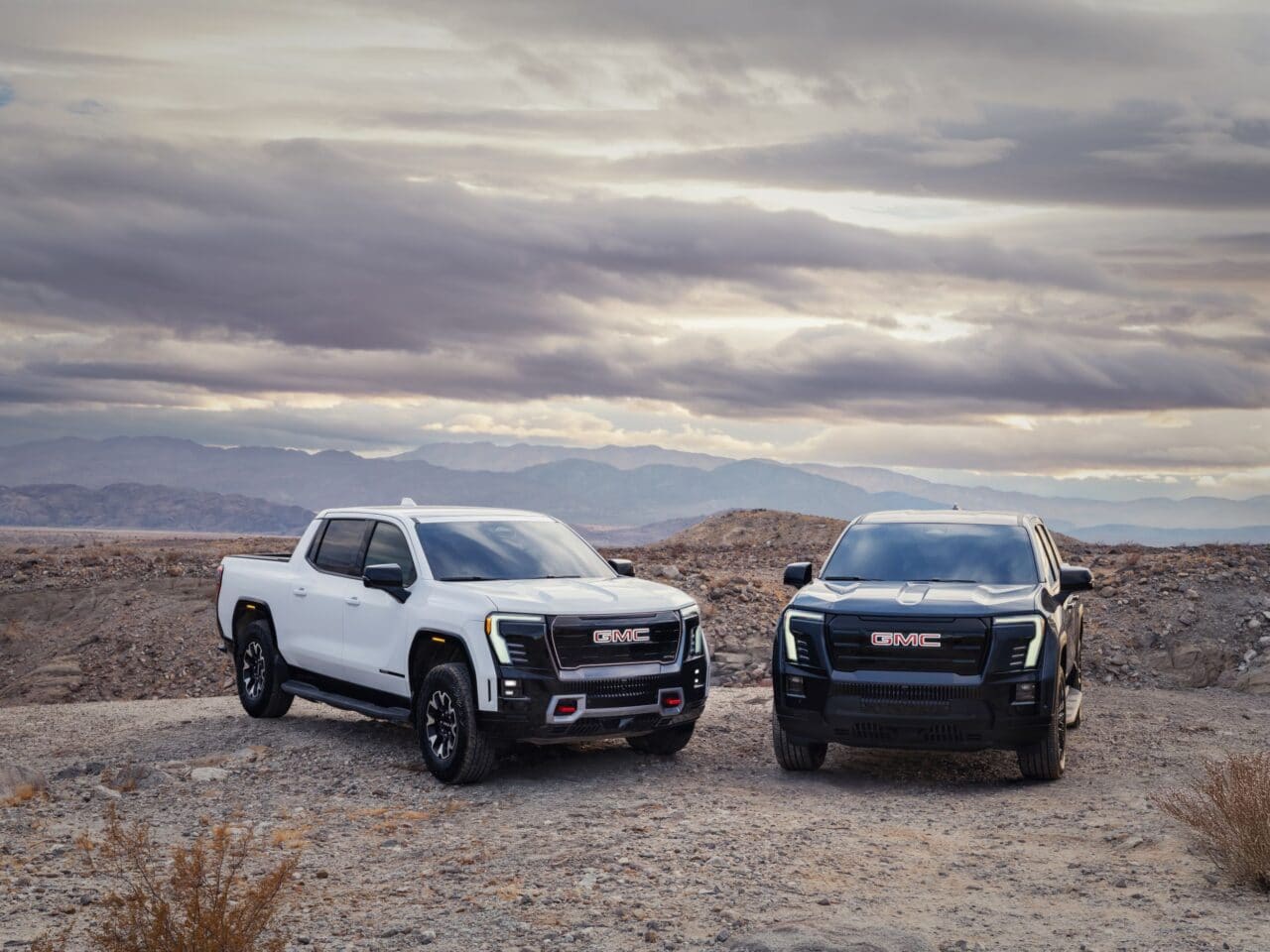 The 2026 Sierra Ev Elevation: Surprisingly Down To Earth 1 view of the 2026 GMC Sierra EV including the AT4 (left) in Summit White, and Elevation (right) in Deep Ocean Metallic.