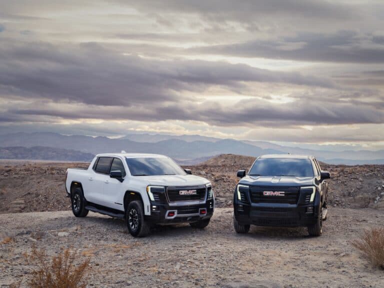 The 2026 Sierra Ev Elevation: Surprisingly Down To Earth 1 view of the 2026 GMC Sierra EV including the AT4 (left) in Summit White, and Elevation (right) in Deep Ocean Metallic.