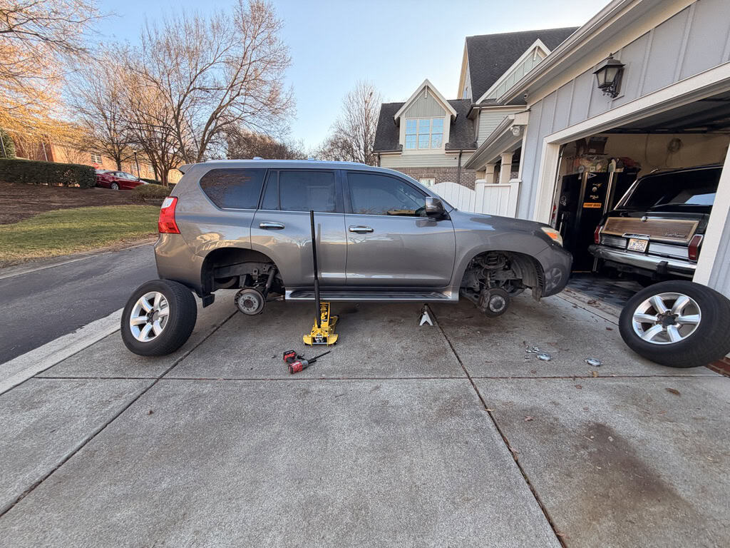 Lexus GX 460 on a car jack getting new Maxxis Razr AT tires installed in the driveway of a home