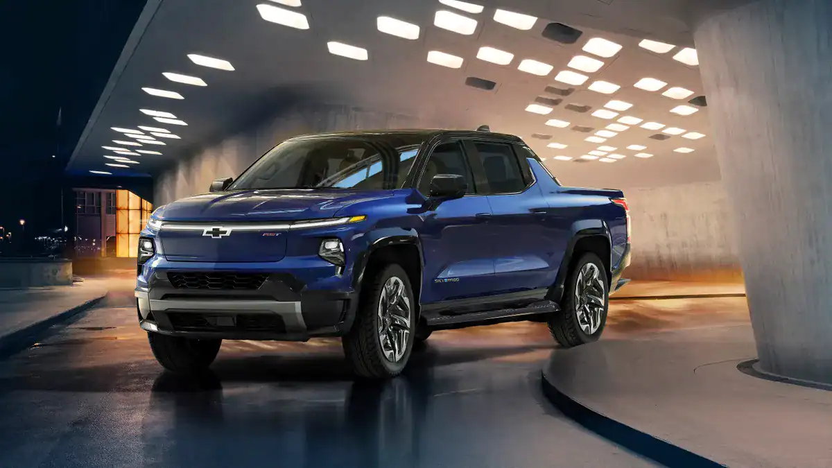 Gm Writes Off Billions, Others Do The Same As Ev Market Tumbles 2 Image of Chevy Silverado EV for article GM writes off billions, where the blue Silverado exits a concrete parking lot.